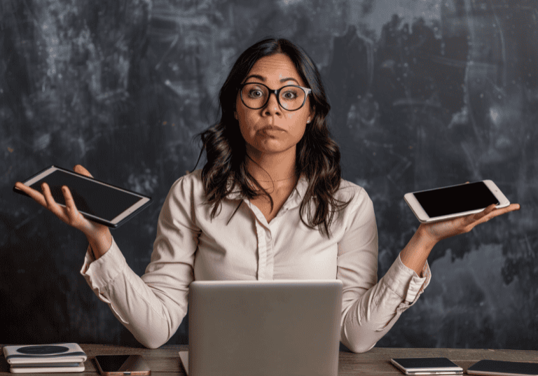 Managing Digital Overload - image of a professional Latina woman holding multiple devices and looking overwhelmed.
